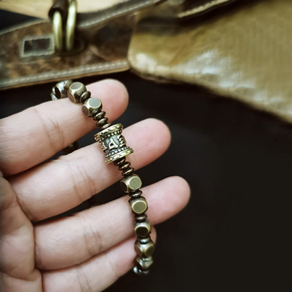 Om Mani Padme Hum Brass Bracelet - Prayer wheel bracelet held over vintage leather bag, artisan jewelry