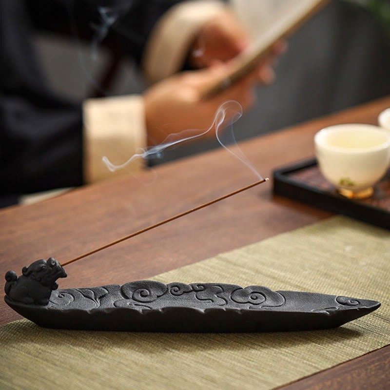Cloud-pattern incense burner with smoke, teacup on dark tray, blurred hand with fan, olive fabric mat – Pixiu ceramic incense holder