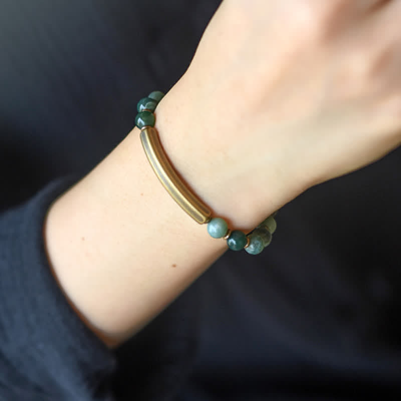 Moss agate bracelet worn on wrist with dark sleeve, green semi-translucent beads with antique brass curved bar and gold spacer beads, nature-inspired jewelry