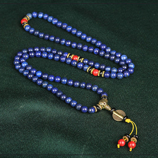 Lapis Lazuli Red Turquoise Tibetan Mala Bracelet in serpentine S-curve on dark fabric, 108 royal blue lapis beads with golden inclusions, red coral accents, black onyx spacers, gold guru bead with braided yellow tassel