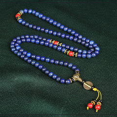 Lapis Lazuli Red Turquoise Tibetan Mala Bracelet in serpentine S-curve on dark fabric, 108 royal blue lapis beads with golden inclusions, red coral accents, black onyx spacers, gold guru bead with braided yellow tassel
