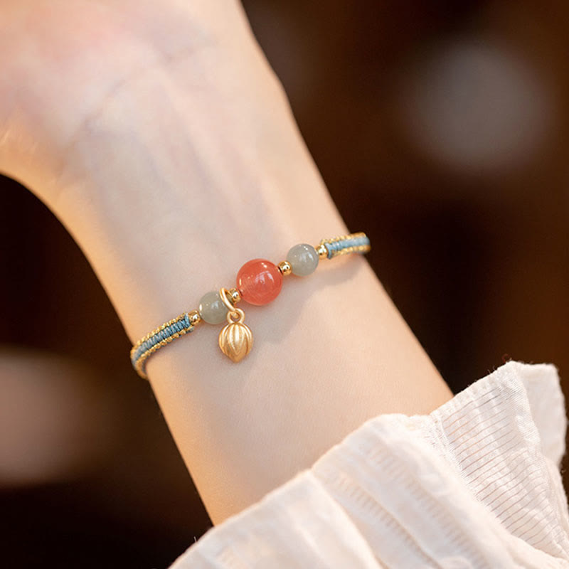 Red Agate Jade Lotus Bracelet – blue gold cord with pink and gray-green beads, lotus pod dangle, fabric sleeve lifestyle photo