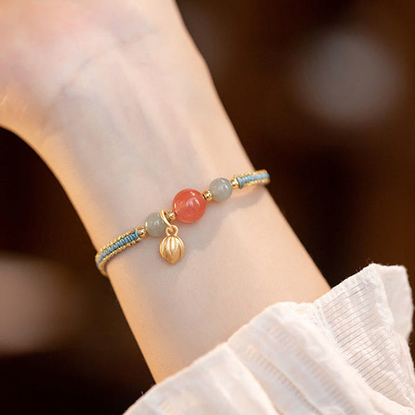 Red Agate Jade Lotus Bracelet – blue gold cord with pink and gray-green beads, lotus pod dangle, fabric sleeve lifestyle photo