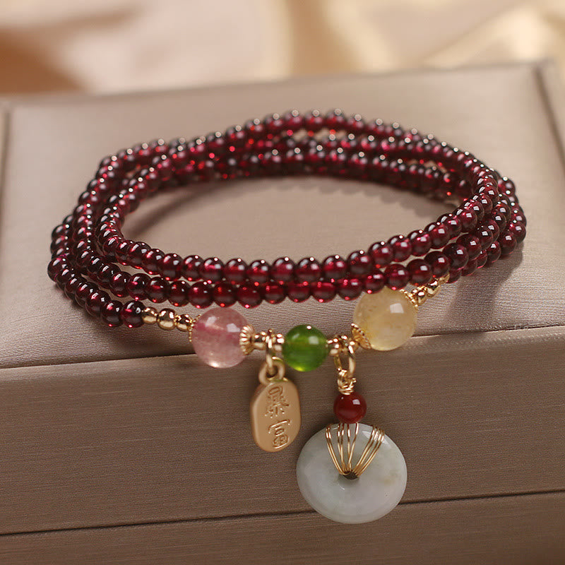 Garnet triple-strand wrap bracelet with bai fu get rich gold tag and jade peace buckle wire-wrapped disc showing garnet beads and mixed semi-precious stone accent beads on display box