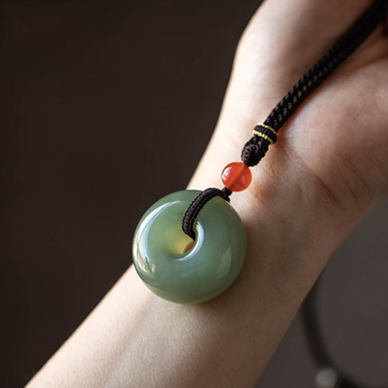 Jade Peace Buckle Lotus Necklace – Black braided cord with jade donut and orange accent bead on hand, jade necklace