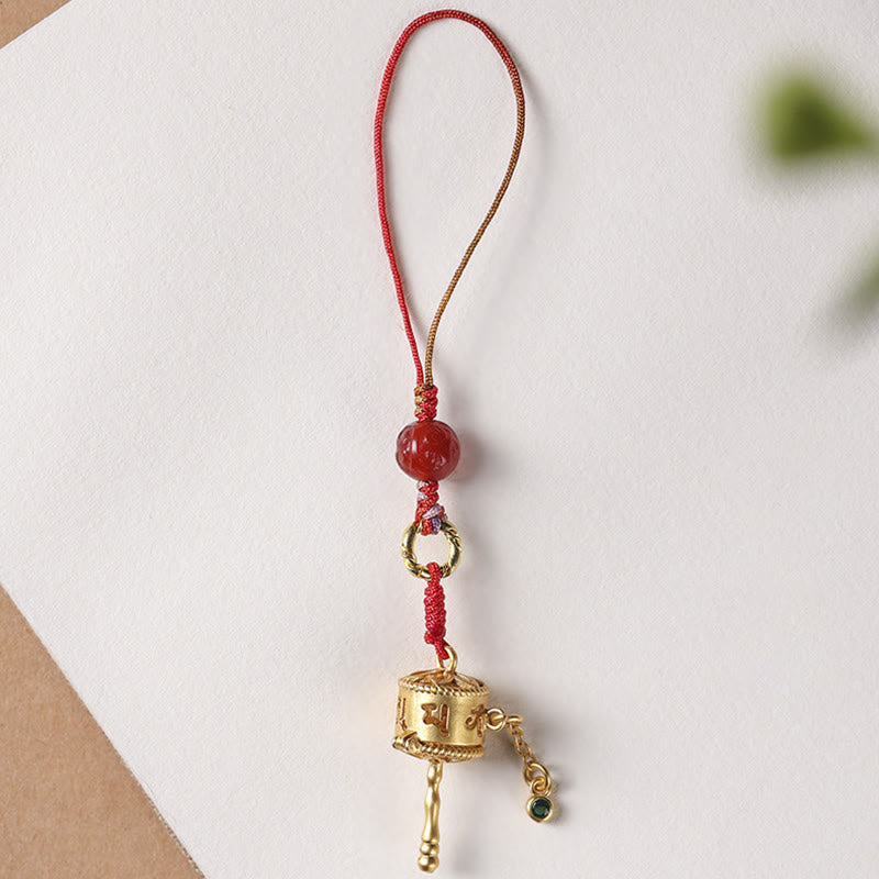 Prayer Wheel Phone Charm – Overhead view on cream background with greenery, red bead pendant