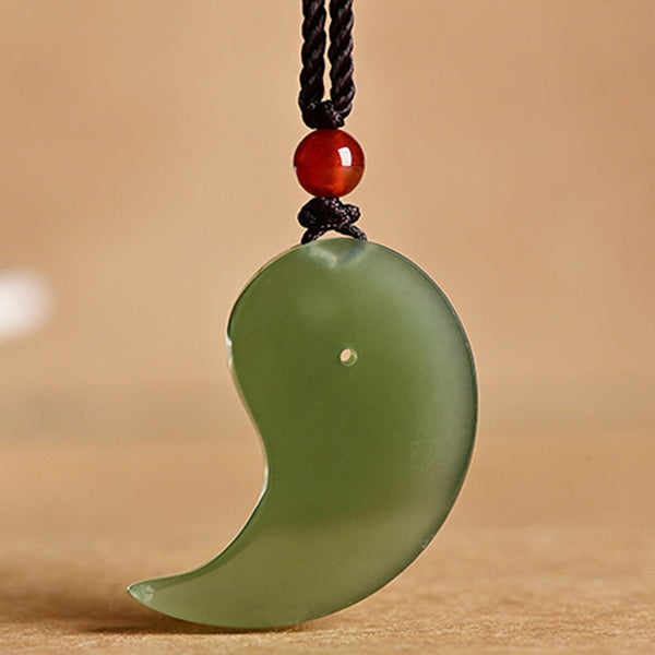 Yin Yang Jade Necklace – Three-quarter view of green jade pendant necklace on black cord, warm background