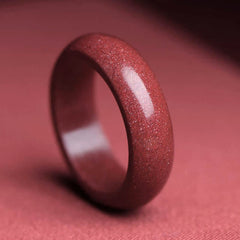 Cinnabar Om Mani Padme Hum Blessing Ring – goldstone ring with copper flecks, polished red-brown band, dusty rose fabric backdrop