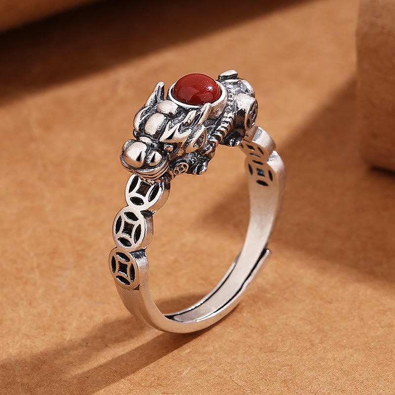 PiXiu Copper Coin Red Agate Ring three-quarter view on kraft paper, silver beast motif, adjustable band, luck