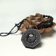 Black Obsidian Yin Yang Pendant Necklace - pendant resting on white background with dried flower prop, bagua obsidian jewelry