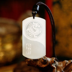 White Jade PiXiu Pendant – White jade pendant with engraved PiXiu and yin-yang on brown cord, wooden branch