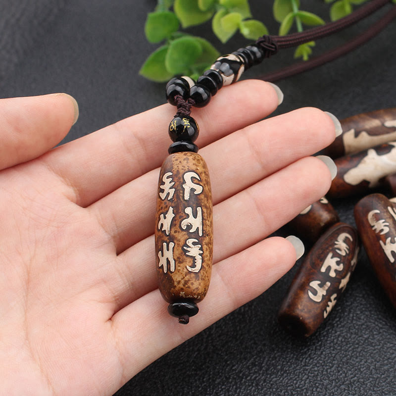 Dzi Bead Necklace – Mantra-inscribed agate pendant held in hand showing carved Tibetan syllables, blessed