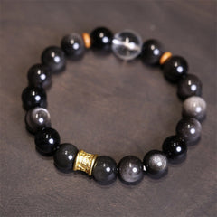 Silver Sheen Obsidian Mantra Bracelet – flat lay showing obsidian beads with gold cylinder charm, crystal bracelet