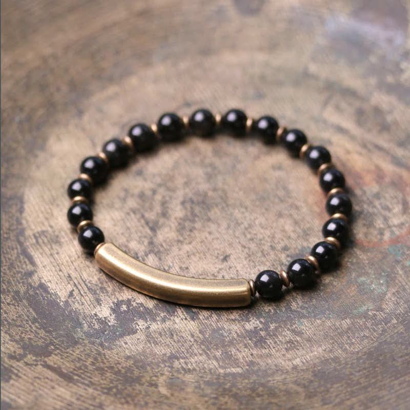 Black obsidian bracelet with antique brass curved bar on distressed wood, glossy black onyx beads with warm gold-toned spacers, minimalist unisex jewelry