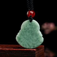 Green Jade Buddha Pendant - mottled jade with black braided cord and red stone bead, dark wood display, front, Luck