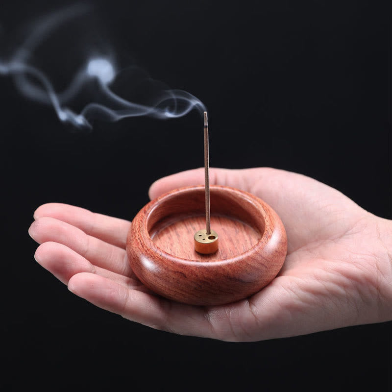 Palm-sized wood incense burner with lit stick smoke on black background, mindful