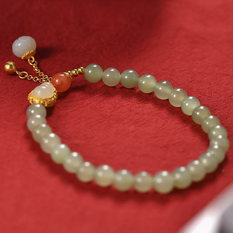 Gourd Lotus Bracelet close-up on crimson fabric, gold setting with jade cabochon and carnelian bead, cultural