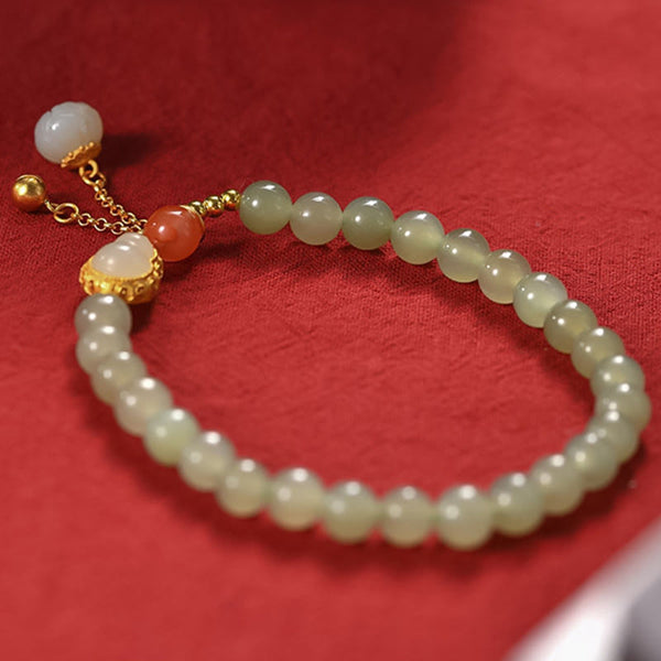 Gourd Lotus Bracelet close-up on crimson fabric, gold setting with jade cabochon and carnelian bead, cultural
