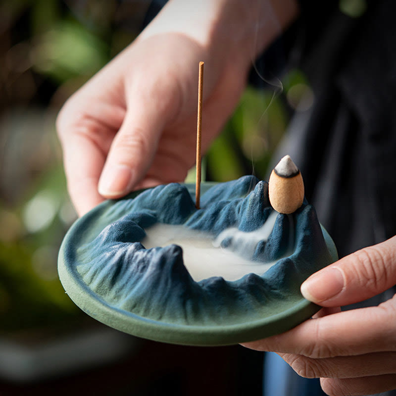 Ceramic Backflow Incense Burner – Hands holding blue mountain dish with smoke flowing like mist, outdoor garden, zen