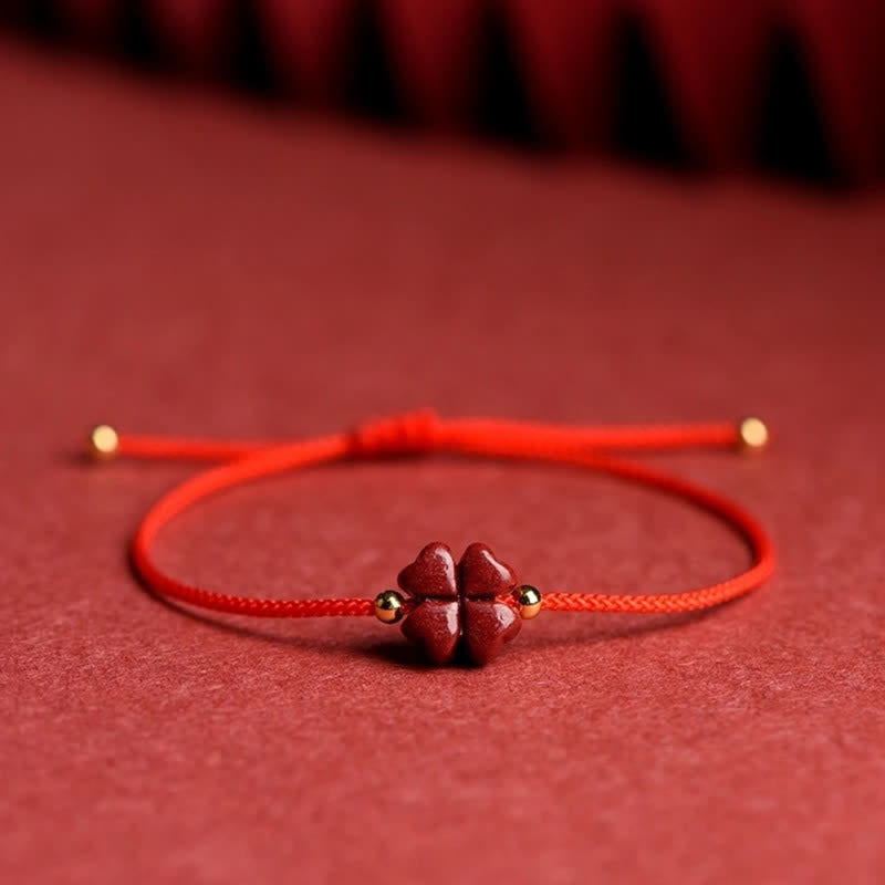Black cord cinnabar four leaf clover bracelet with dark red carved charm gold spacer beads and adjustable sliding knot on deep burgundy red textured fabric background