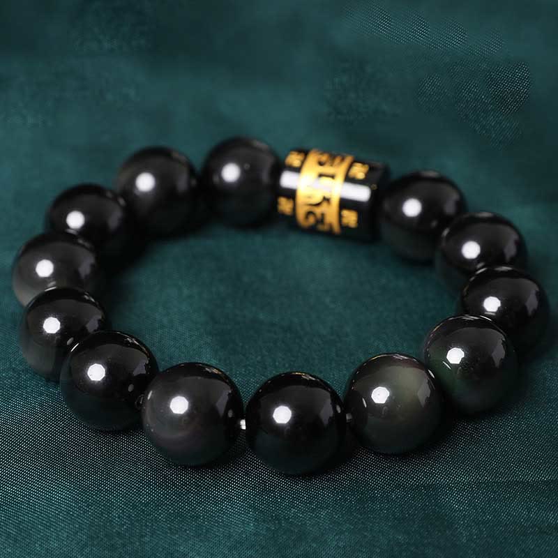 Rainbow Obsidian Bracelet – Angled view of black bead bracelet with gold mantra charm on teal silk, feng shui jewelry