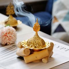 Gold Alloy Mini Incense Burner – ornate filigree dome lid with rising smoke on natural wood logs, incense burner home decor
