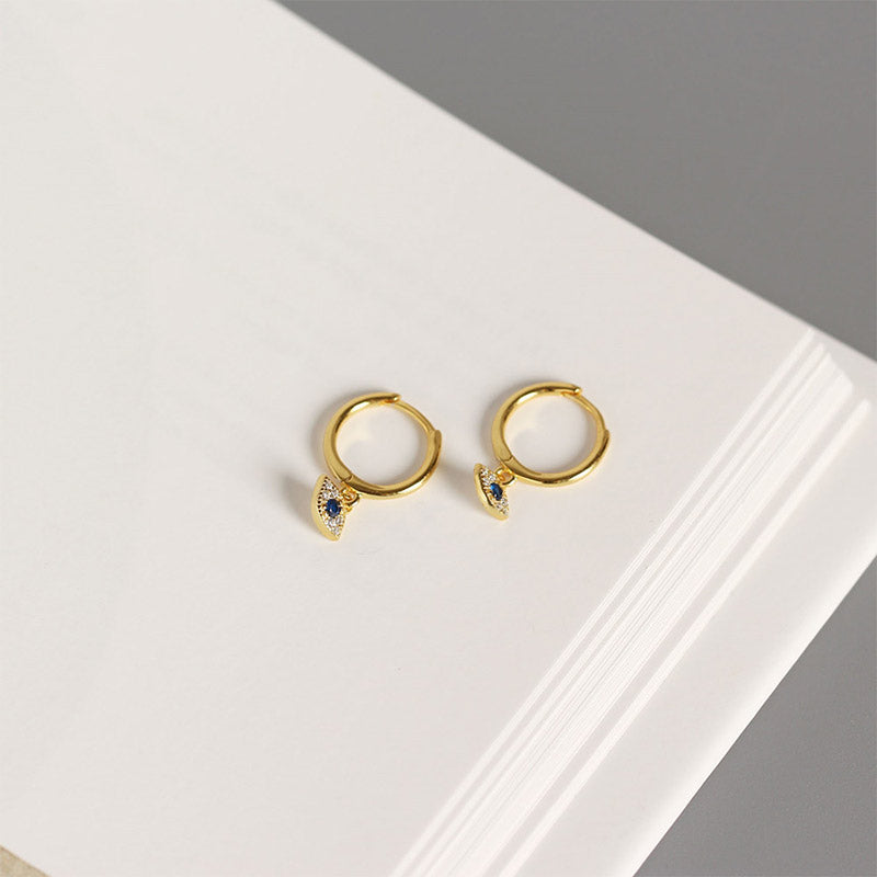 Gold Evil Eye Huggie Earrings with Pavé Blue Evil Eye Charm on White Background