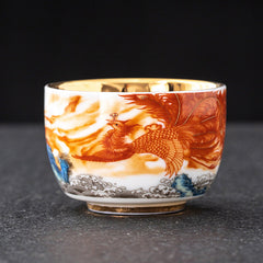 Dragon Phoenix Crane Gilt Ceramic Teacup – hand-painted red phoenix with golden clouds and cobalt blue wave base, gold interior, ceremonial