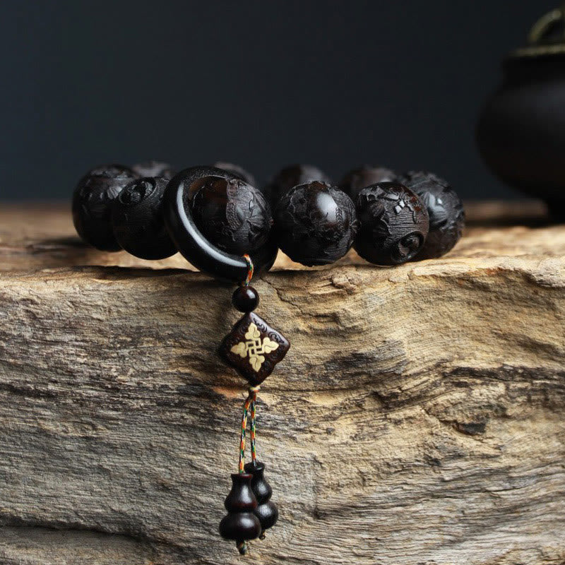 Ebony Wood Yin Yang Gourd Balance Bracelet - side view showing carved relief patterns and ring spacer on rustic wood, carved wood bracelet
