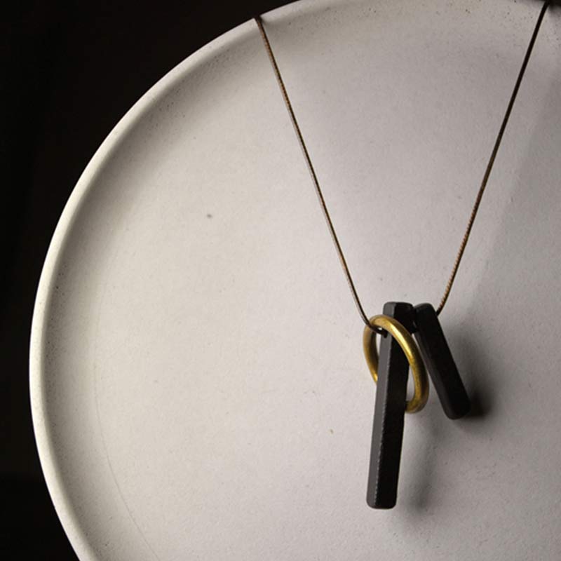 Zen Circle Ebony Wood Necklace - black bar and gold ring pendant on ceramic plate, dramatic shadow