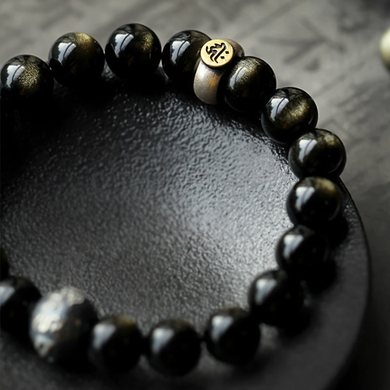 Zodiac Natal Buddha Obsidian Silver Bracelet - Shallow focus on gold mantra charm with obsidian beads
