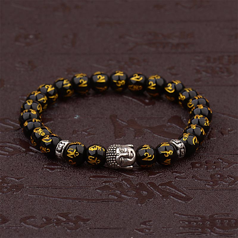 Tibetan Buddha Om Mani Padme Hum Amulet Bracelet - faceted black obsidian beads with gold Om Mani Padme Hum, silver Buddha head amulet, silver decorative spacer beads, wrist mala on dark stone with wooden display props