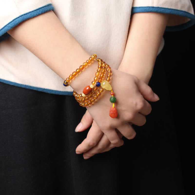 Citrine Mala Bracelet – Hand holding citrine mala strands with amber guru bead, dark backdrop