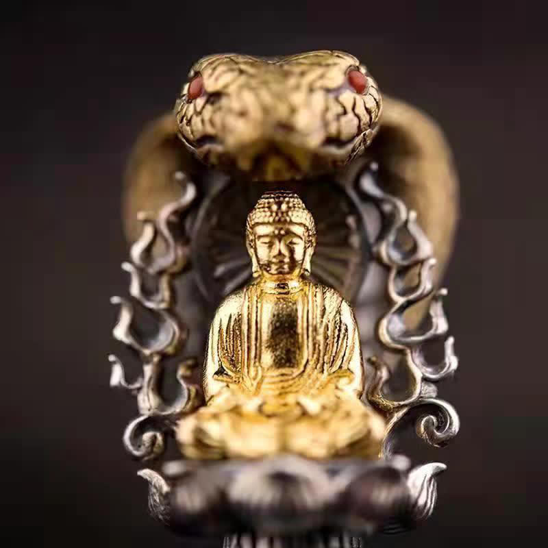 Tibetan Vajra Rotating Pendant – Gold Buddha figure with naga cobra hood and red gemstone eyes on dark silver lotus base, black background shallow depth, frontal