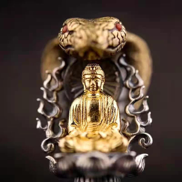Tibetan Vajra Rotating Pendant – Gold Buddha figure with naga cobra hood and red gemstone eyes on dark silver lotus base, black background shallow depth, frontal