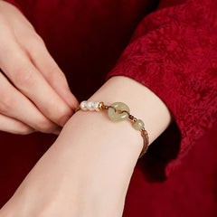 Hetian Jade Pearl Peace Buckle Bracelet – pale green jade bi disc with white pearls on model wrist, red textured silk background