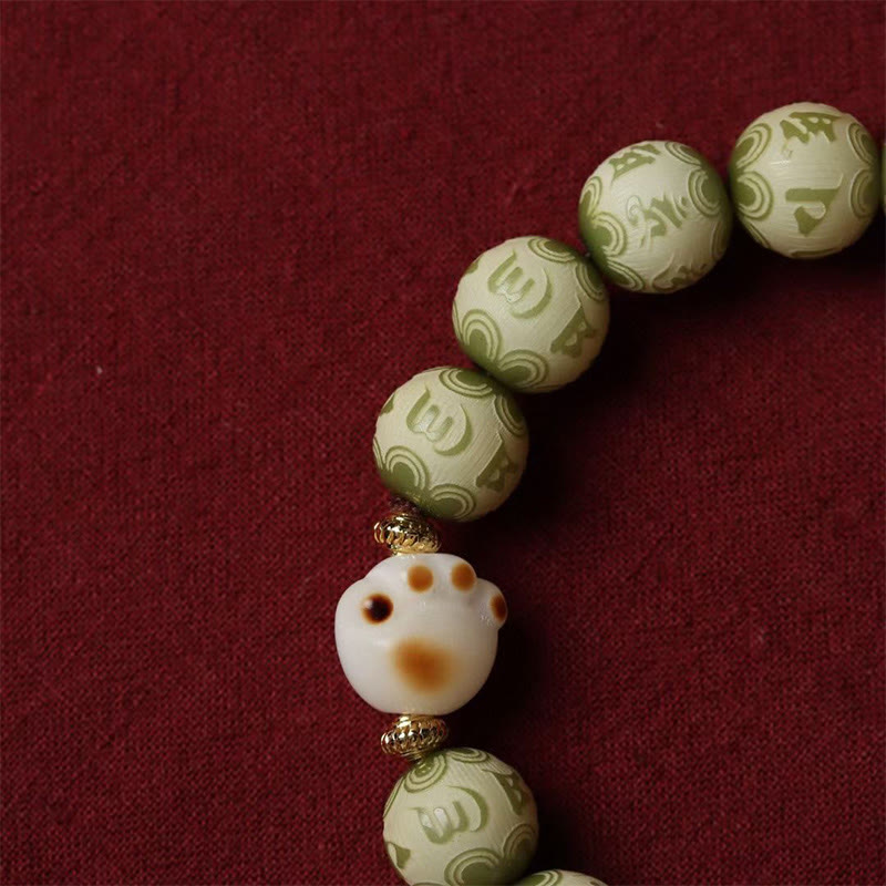 Bodhi Seed Bracelet – Close-up of white cat paw bead with gold spacers among green engraved beads, cat paw bracelet