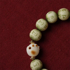Bodhi Seed Bracelet – Close-up of white cat paw bead with gold spacers among green engraved beads, cat paw bracelet
