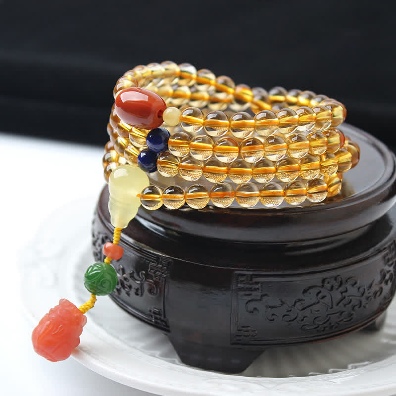 Citrine Mala Bracelet – Citrine mala coiled on carved wooden stand with coral PiXiu charm