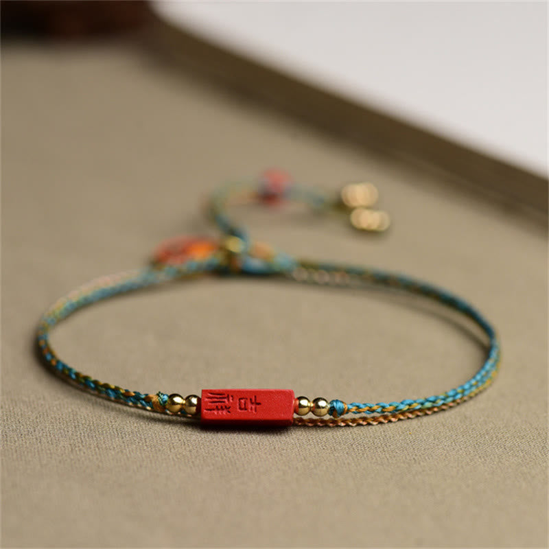 Cinnabar Braided Bracelet - Red rectangular bead on turquoise gold cord, linen backdrop