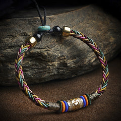 Tibetan Five-Color Bracelet – side view of braided threads with gold barrel charm on textured rock, Tibetan artisan craft