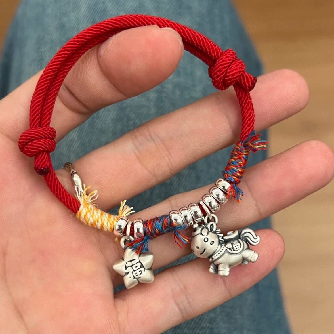 Horse Red String Bracelet – Hand holding red cord bracelet with silver horse charm and fortune star, 2026