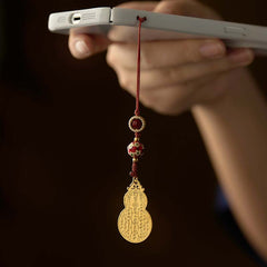 Antique gold gourd phone charm hanging from white smartphone held in hand