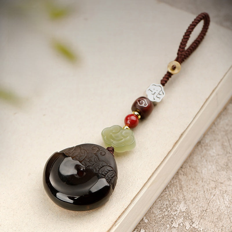 Pixiu Keychain – ice obsidian disc with brown cord and jade cloud on beige book, protection amulet Main image