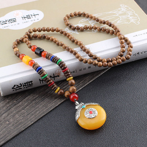 Wenge Mala Necklace – yellow pendant mala draped over Chinese book cultural spiritual jewelry, wood surface