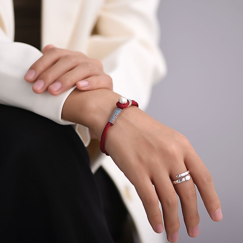 Persimmon Cord Bracelet – Red cord bracelet worn on wrist with white sleeve, minimalist luck jewelry
