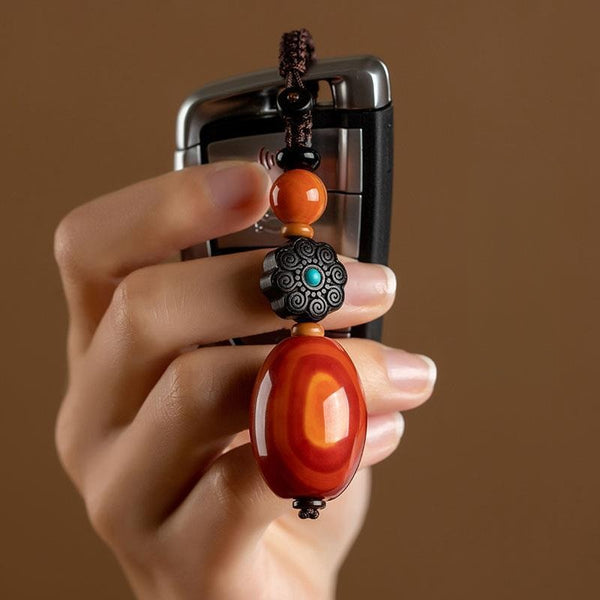 Red Agate Car Keychain – hand holding red agate and ebony flower charm with car key, brown studio background