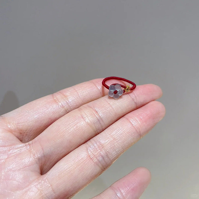 Red String Flower Ring – delicate red string ring resting on open palm, translucent white flower, gold coin detail, close-up view