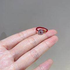 Red String Flower Ring – delicate red string ring resting on open palm, translucent white flower, gold coin detail, close-up view