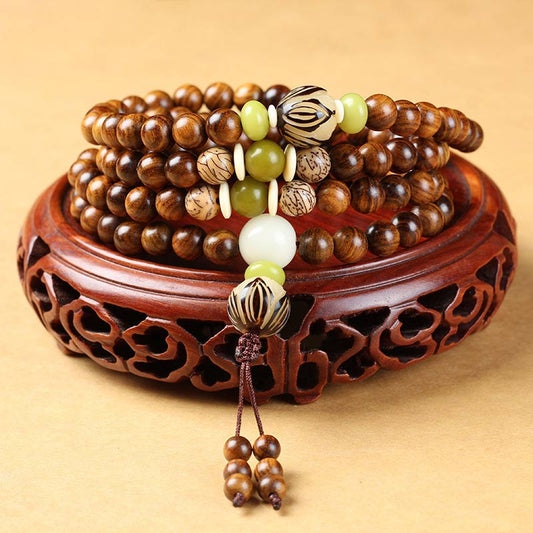 Tibetan Rosewood Bodhi Seed Mala Bracelet with green jade accent beads and carved guru bead, displayed on carved wooden stand, front view, traditional 108-bead meditation necklace wrap bracelet with brown tassel